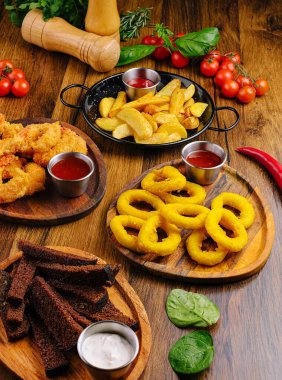 Soğan halkaları, ekmek çubukları ve patates parçaları da dahil olmak üzere çeşitli kızarmış atıştırmalıklar taze sebzeler ve otlarla çevrili daldırma soslarıyla ahşap tahtalarda güzelce düzenlenmiştir..