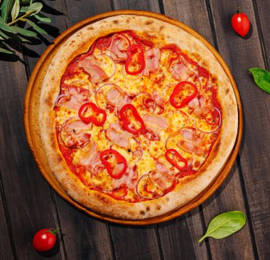 Yeni pişmiş bir pizza, erimiş peynir, jambon ve pepperoniyle süslenmiş dilimlerin sergilendiği ahşap bir tabakta duruyor. Çeri domatesleri ve otlar tabağın etrafını sararak cazibesini arttırıyor..