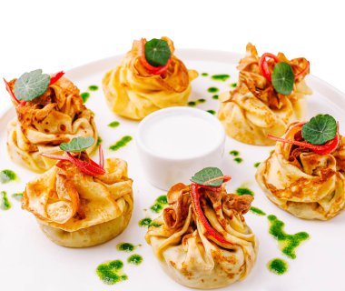 Yeşil otlar ve kırmızı biberlerle süslenmiş beyaz bir tabakta altı tane güzel işlenmiş hamur işi düzenleniyor. Yüzmek için ortaya küçük bir kase sos konur..