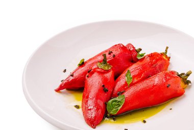 Taze hazırlanmış kırmızı biberler temiz beyaz bir tabağa oturur, zeytin yağı serpiştirilir ve canlı otlarla süslenir, lezzetli bir mutfak yaratımı sergilenir..