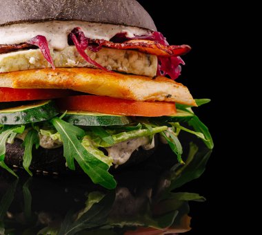 Bu yemek eşsiz malzemelerle yapılmış çarpıcı bir siyah burger içeriyor. Üstünde marul, domates ve soğan gibi taze sebzeler var. Modern bir mutfak sunumu sergileniyor..