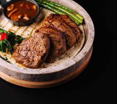 Sulu ızgara biftek dilimleri zengin bir sos ve taze yeşil sebzelerle birlikte ahşap bir tabakta zarif bir şekilde düzenlenir. Güzel bir yemek için harika bir sunum..