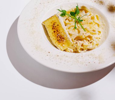 Bol soslu, taze otlarla süslenmiş güzel bir tabak makarna. Tabakta kızarmış peynirin yanında iştah açıcı bir mutfak deneyimi sunuluyor..