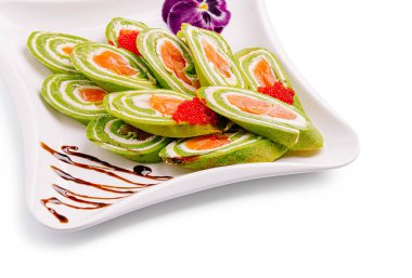 Narin suşi ruloları beyaz bir tabakta ustalıkla düzenlenir. Canlı yeşil katmanlar, sanatsal çiseleme ve yenilebilir çiçeklerle tamamlanmış somon ve yumurtayı ön plana çıkarıyor..