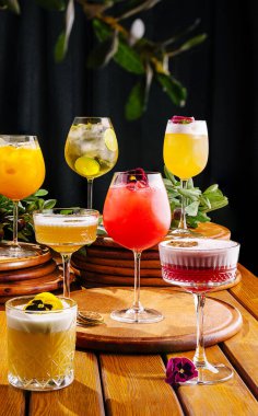 Yuvarlak ahşap altlıklarda canlı bir kokteyl dizisi sunuluyor. Her içki taze meyve ve çiçeklerle süslenir, canlı bir bar atmosferi sergiler sosyal toplantılar için mükemmeldir..