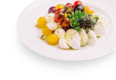Canlı bir salatada çeşitli üzümler ve taze mikro yeşilliklerle çevrili beyaz mozzarella topları bulunur. Yemek zarif bir şekilde büyük beyaz bir tabakta sunuluyor. Renkli malzemelerini vurguluyor..