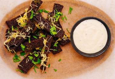 Siyah ekmek çubukları taze otlar ve limonla kaplı bir tabakta sanatsal olarak düzenlenir. Küçük bir kase kremalı sos yemeği tamamlar, onu iştah açıcı ya da aperatif yapar..