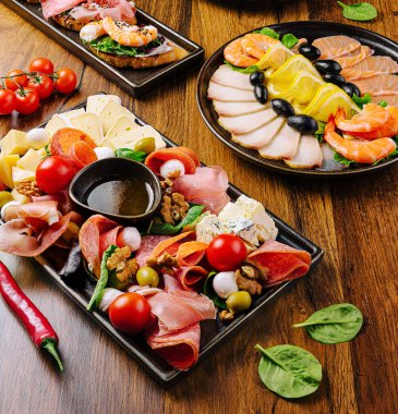 Tahta tabaklar üzerinde çeşitli et, peynir, zeytin ve vişneli domateslerin canlı bir gösterisi güzel bir şekilde düzenlenmiştir. Taze yeşillikler ve küçük bir kase zeytinyağı iştah açıcı bir cazibe katıyor..