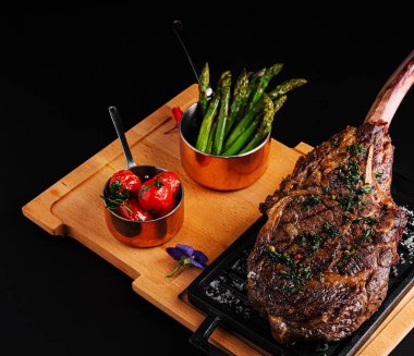 Izgara domates ve kuşkonmazın yanında güzel bir kaplanmış tomahawk bifteği sunulur. Tabak otlarla süslenmiş, marifetli mutfak sanatları ve canlı renkler sergileniyor..