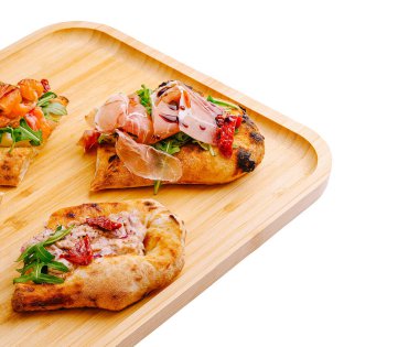 Tahta tepside canlı yeşillikler, füme somon ve pişirilmiş etle kaplı üç tane açık yüzlü sandviç var. Bu enfes sunumda taze yemek yaratıcılığı sergileniyor.