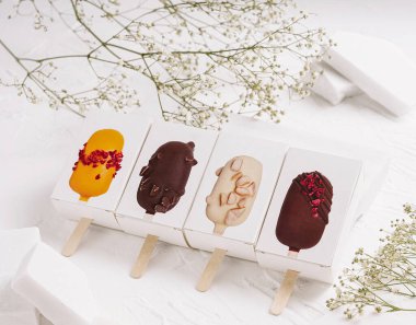 Renkli donmuş tatlılar çubukların üzerinde sunulur, eşsiz tatlar ve malzemeler sergilenir. Onlara narin beyaz çiçekler eşlik eder. Çekici bir görsel düzenleme oluştururlar..