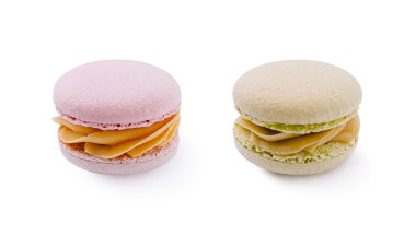 İki badem kurabiyesi yan yana durur, canlı renkler içerir. Biri meyveli kremayla dolu pembe, diğeri yeşil, hafif, kremalı, tatlı bir deneyim davet ediyor..