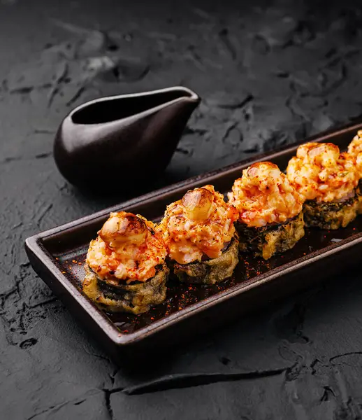 Izgara karidesli lezzetli suşi sade, koyu bir tabakta oturur. Yemeklere eşlik eden küçük bir sos kabı, güzel bir yemek deneyimi için uygun zarif sunumu vurgular..