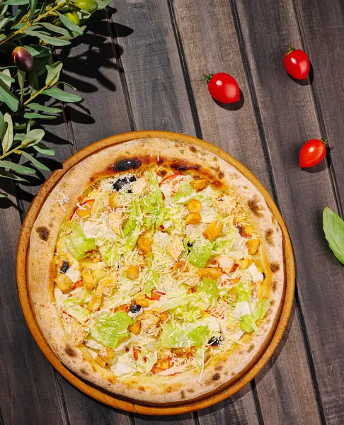 Taze marul, sebze ve peynirden oluşan ağız sulandıran bir pizza rustik ahşap bir masaya yerleştirilir. Pizzayı çevreleyen kiraz domatesleri ve zeytinler, onun canlı görünümünü güçlendirir..