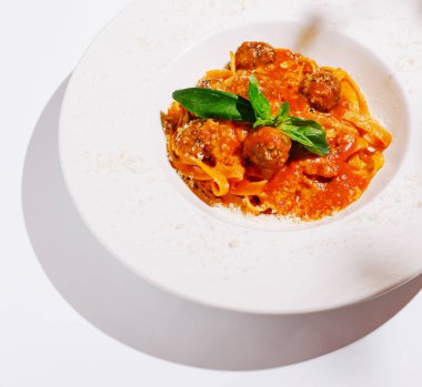 Lezzetli köfteli, domates soslu ve taze fesleğenli bir tabak makarna. Beyaz arka plan yemeğin canlı renklerini vurgular, iştah açıcı bir görünüm yaratır..