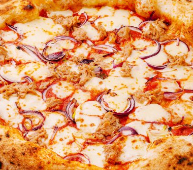 Taze pişmiş pizza eritilmiş peynir, lezzetli ton balığı ve dilimlenmiş kırmızı soğanla kaplıdır. Yemek sıcak bir mutfakta servis ediliyor, davetkar atmosferi ve lezzetli aromayı vurguluyor..