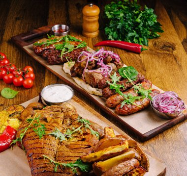 Tahta tahtalarda taze sebze ve soslarla birlikte çeşitli ızgara etler sergileniyor. Kurulumda otlar ve domateslerle süslenmiş kırsal ahşap bir masa yer alıyor..