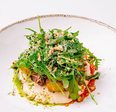 Canlı bir salatada mevsimlik sebzeler ve ezilmiş fındıklarla kaplı taze roka bulunur. Renkli sargılar görsel cazibe katar, sağlıklı bir yemek için ideal bir yemek yaratır..