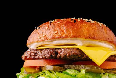 Eritilmiş peynirli nefis bir sığır burger, taze marul, domates ve susamlı çöreğin içine yerleştirilmiş turşu. İçindekiler parlak, siyah bir zemin üzerinde parlıyor..