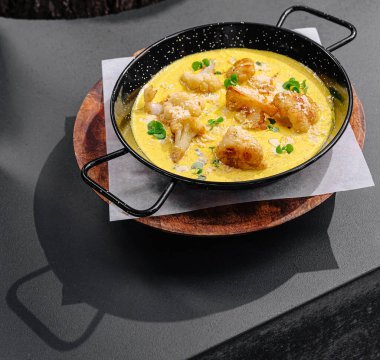 Kremalı sosta pişirilmiş taze et ve sebzelerden oluşan lezzetli bir yemek siyah bir tavada oturur. Tabak ahşap bir yüzeye yerleştiriliyor, canlı renkleri vurguluyor..