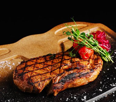 Kusursuz ızgara bir biftek, kiraz domatesleri ve mikroyeşilliklerle süslenmiş kırsal bir tabakta sergilenir. Sunum, kurum izleri ve sulu dokuyu vurgular.