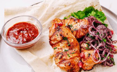 Lezzetli ızgara tavuk parçaları taze soğan salatası ve zengin sosla birlikte bir porsiyon taze ekmek üzerine oturur. Yemek, cazip bir sunum için yeşil otlarla süslenmiş..