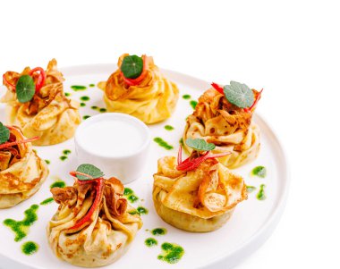 İçi et dolu iştah açıcı gözlemeler, keseye bağlanmış, sosla servis edilmiş, beyaz tabakta otlar, gurme yemekler..