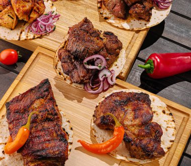 Cızırdayan et parçaları ahşap tahtalarda, kırmızı soğan ve kırmızı biber aksanlı taze tortilla ile düzenlenir. Bu canlı gösteri, şenlikli bir yemeğe lezzetli bir bakış sunuyor..