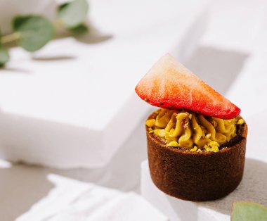 Bu tatlı, üzerinde taze çilek dilimi olan kremalı şam fıstığı kremalı zengin bir tart içeriyor. Parlak, minimalist arka plan canlı renklerini geliştirir..