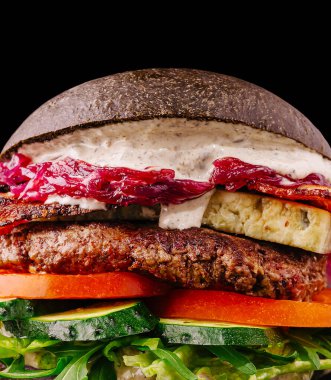 Bu hamburgerde sulu sığır etli börek, taze marul, domates, salatalık katmanları ve lezzetli bir sos ve tatlı böğürtlen reçeli ile kaplı çarpıcı bir siyah çörek var..