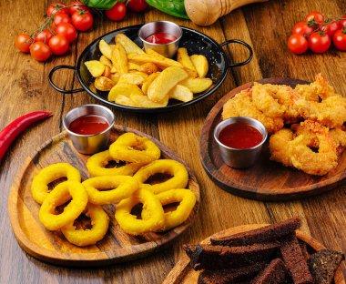 Tahta tabaklar üzerinde çeşitli kızarmış atıştırmalıklar altın soğan halkaları, çıtır çıtır karides ve patates dilimleri sergileniyor..
