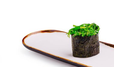 Deniz yosunundan yapılmış ve canlı yeşil yosun salatasıyla dolu bir suşi rulosu basit bir Japon tabağında oturup yemeğin tazeliğini ve sunumunu sunar..