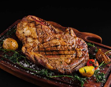 Ağız sulandıran ızgara biftek ahşap bir tabakta sunulur. Kızarmış patates ve renkli sebzelerle birlikte, et severler için davetkar bir aşçılık deneyimi sunuyor..