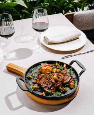 Sulu biftekler, renkli sebze taraflarıyla çevrili, cızırdayan demir bir tavada dinleniyor. İki zarif şarap kadehi şık bir restoranda güzel bir masada bekliyor..