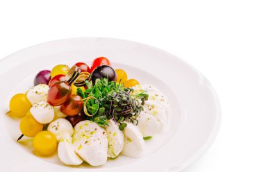 Canlı bir salatada çeşitli renklerde kiraz domatesleri ile çevrili taze mozzarella topları bulunur. Mikroçimler yemeğin sunumunu geliştirmek için hassas bir dokunuş ekliyor..