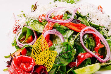 Canlı bir salatada taze ıspanak, kavrulmuş kırmızı biber, ince soğan dilimleri ve bir tutam peynir bulunur. Parlak renkler ve dokular sağlıklı bir yemek için davet edici bir sunum oluşturur.