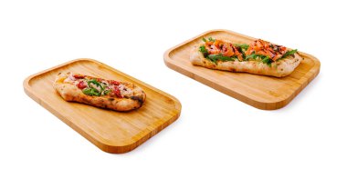 İki çeşit düz ekmek, ahşap tepsilerde güzelce sıralanmıştır. Biri lezzetli et ve otlarla kaplanırken, diğerinde taze sebze ve deniz ürünleri, canlı renkler sergileniyor..