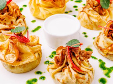 Lezzetli dolgulu, yeşil bitkisel yağ damlaları ve kırmızı biber garnitürlü beyaz bir tabakta servis edilen nefis krep kesesi.