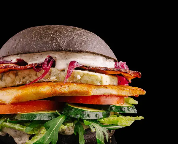 Yükselen bir siyah hamburger, kıtır kıtır pastırma, ızgara tavuk, taze marul, domates, salatalık ve kremalı sos katmanları içerir..