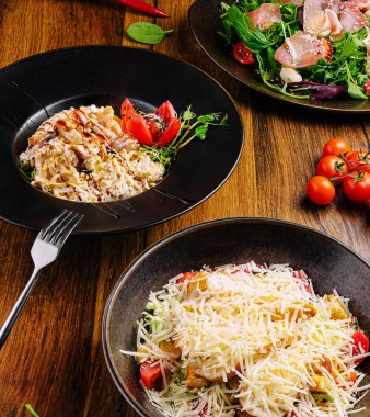 Siyah tabaklar üzerinde güzel bir canlı salata ve lezzetli bir makarna tabağı sunuluyor. Kiraz domatesleri ve yeşiller öğle yemeği sırasında ahşap yemek düzenine tazelik ekler..