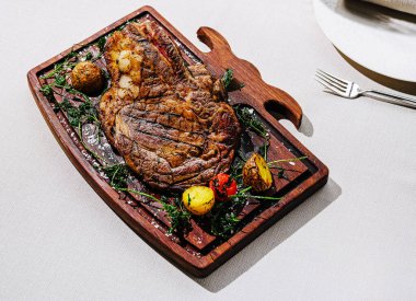 Lezzetli bir pişmiş biftek ahşap bir tepside sunulur, yanında da kızarmış sebzeler. Yemek, zarif bir yemek ortamında zengin lezzetleri ve çekici dokuları ön plana çıkarıyor..