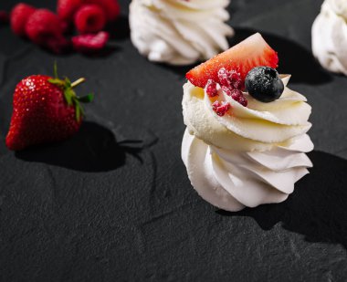 Taze çilek, yabanmersini ve ahududu ile süslenmiş lezzetli kremalar koyu bir taş yüzeyde dinleniyor..