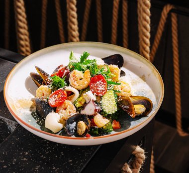 Canlı bir yemek, bitkiler ve peynirle süslenmiş karides ve midye de dahil olmak üzere renkli bir deniz ürünleri çeşidine sahiptir. Zarif bir sahil restoranına yerleştirilmiştir..