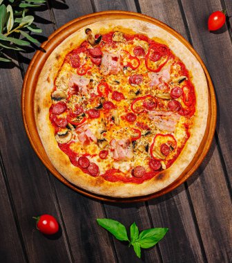 Biberli ve mantarlı taze pişmiş pizza ahşap bir masada oturur. Çeri domatesleri ve fesleğen yaprakları tabağın etrafını sararak canlı ve iştah açıcı bir sunum oluşturuyor..