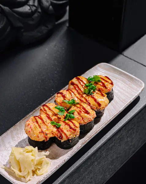 Izgara deniz ürünleri ile süslenmiş taze otlarla süslenmiş suşi rulolarının tadını çıkarmak. Havalı bir tabakta sunulan, turşulu zencefil ile tamamlanmış mükemmel bir yemek..