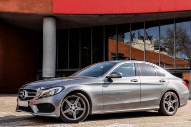 Alaşımlı tekerlekleri olan gümüş renkli bir MercedesBenz CClass bir binanın önüne park edilmiş, parlak tasarımını ve otomotiv aydınlatmasını sergiliyor.