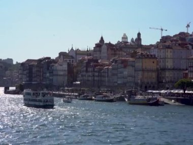 Huzurlu bir tekne, arkasında canlı bir şehir silüeti olan bir nehirde süzülüyor. Su şehir manzarasını yansıtıyor, doğa ve şehir yaşamını birleştiriyor.