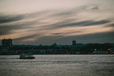 Bir tekne, sakin bir su kütlesinin üzerinde nazikçe yüzüyor. Arka planda güzel bir manzara yaratıyor.