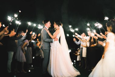 Akşam nikâhı. Gelin ve damat ışıkların ve fenerlerin arkasında el ele tutuşuyorlar.