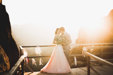 Yeni evli çift, gelin ve damat öpüşüyor, mükemmel dağ manzarasında sarılıyorlar, mavi gökyüzü.